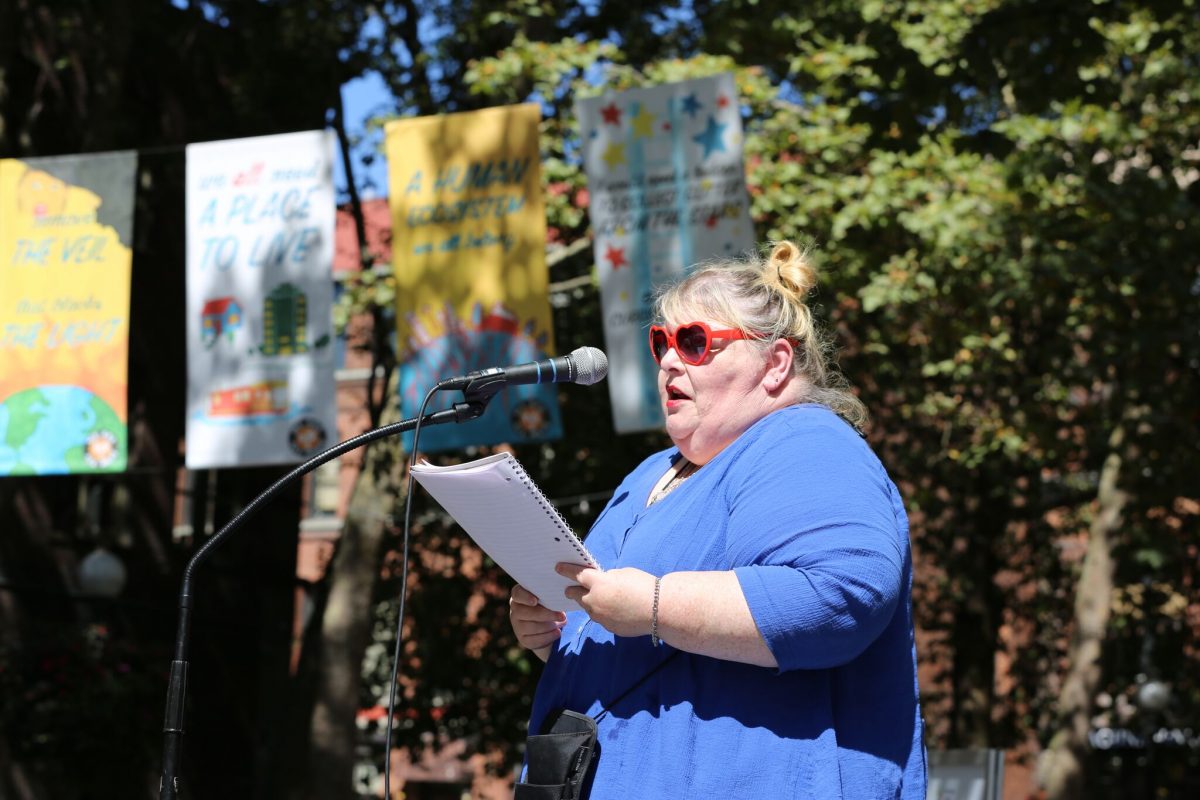 A student artist reading her poem in front of the We Are All Here banner. Photo credit: Path with Art